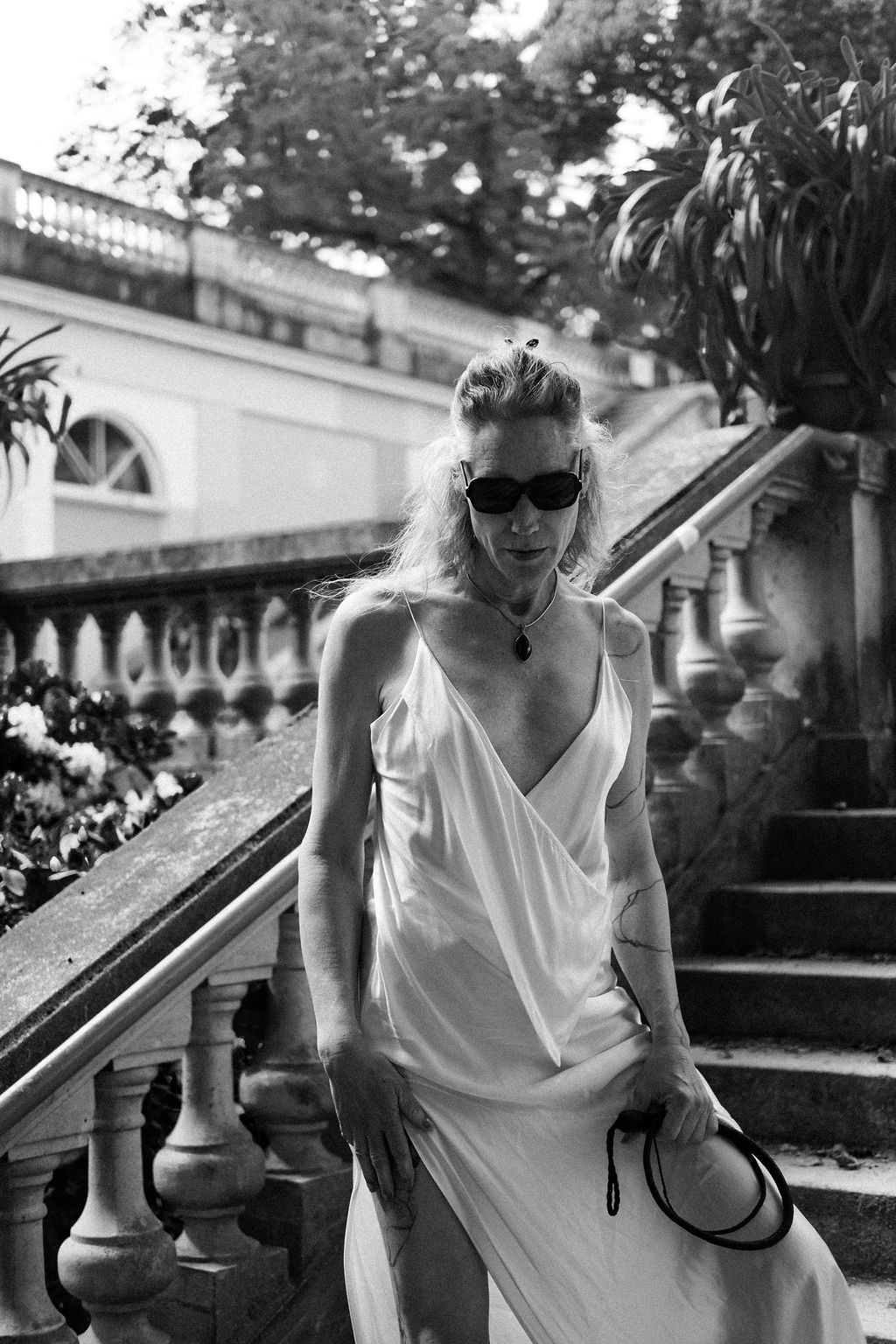 Valentina Dellagravis in a white dress on stone steps, elegant and composed, holding a leash.